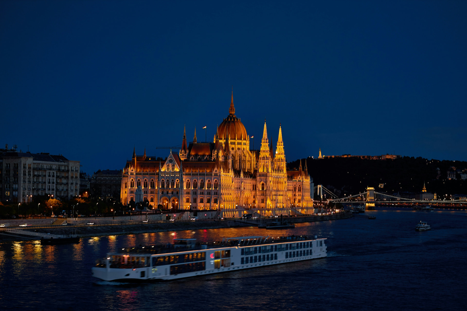 River cruise ship passing the illuminated Hungarian Parliament in Budapest at dusk